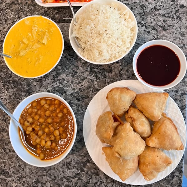 An overhead view of Cali Tardka Indian takeaway dishes, including samosas, rice, chana masala, and yellow curry.