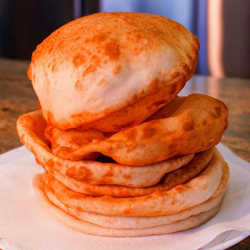 A stack of golden-brown, fluffy Indian puri bread on a white napkin.