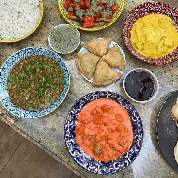 Overhead view of a Cali Tarka Indian takeaway spread with curries, rice, samosas, and sauces.