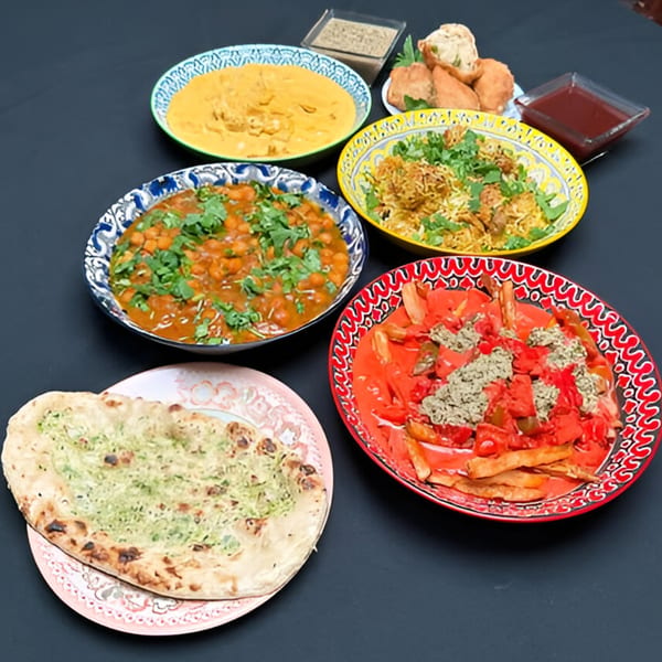A spread of Indian dishes including naan, chickpea curry, biryani, and fries with red sauce.